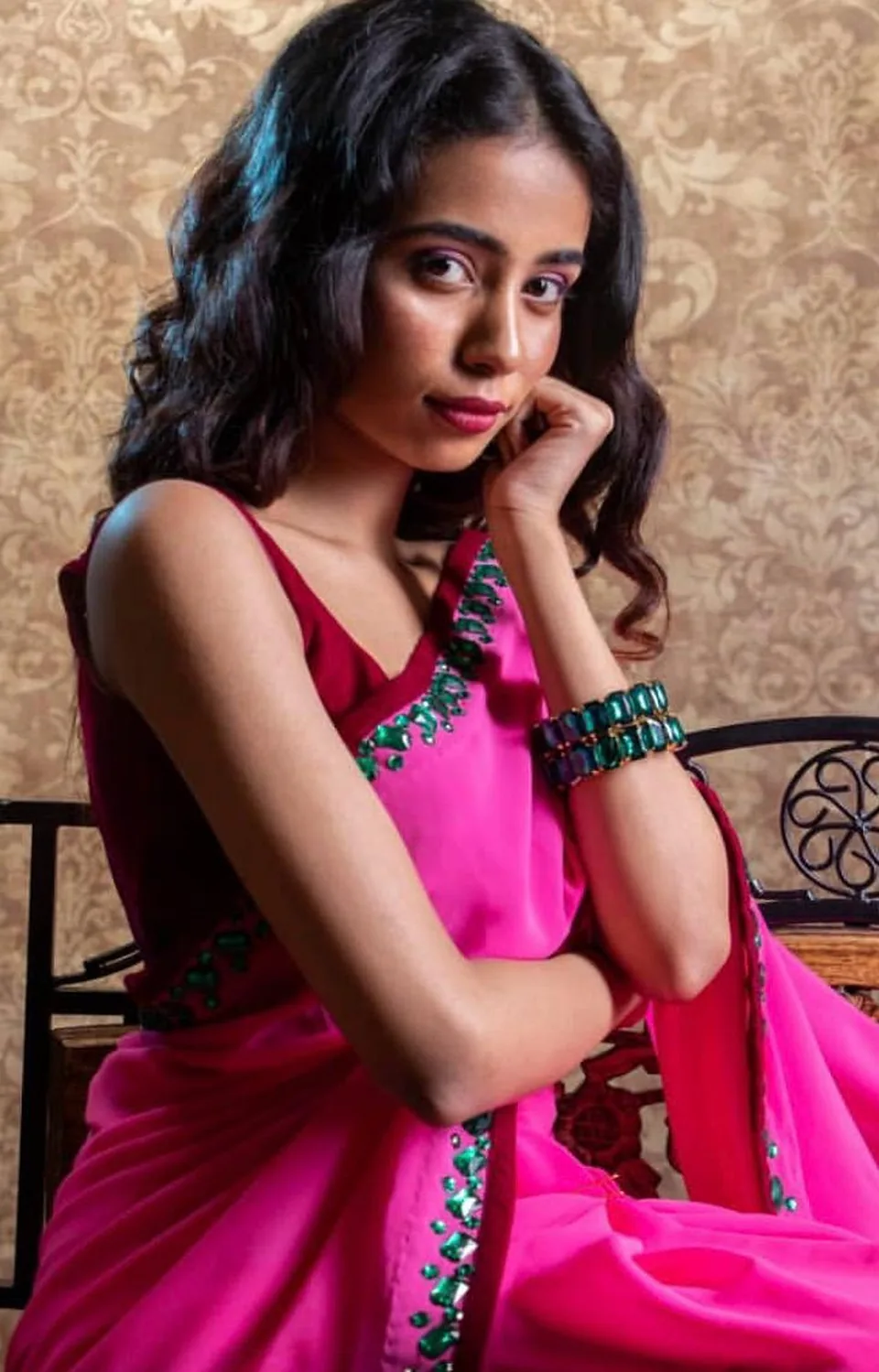 Model seated in the rani pink saree, chin resting on her hand, wearing emerald-green bangles.