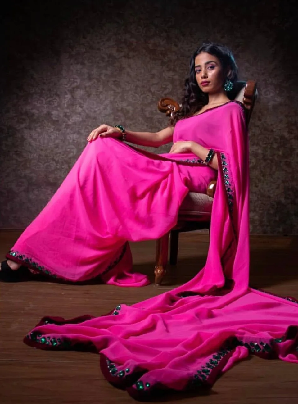 Model seated on a carved chair, the long pallu of the saree pooling on the floor.